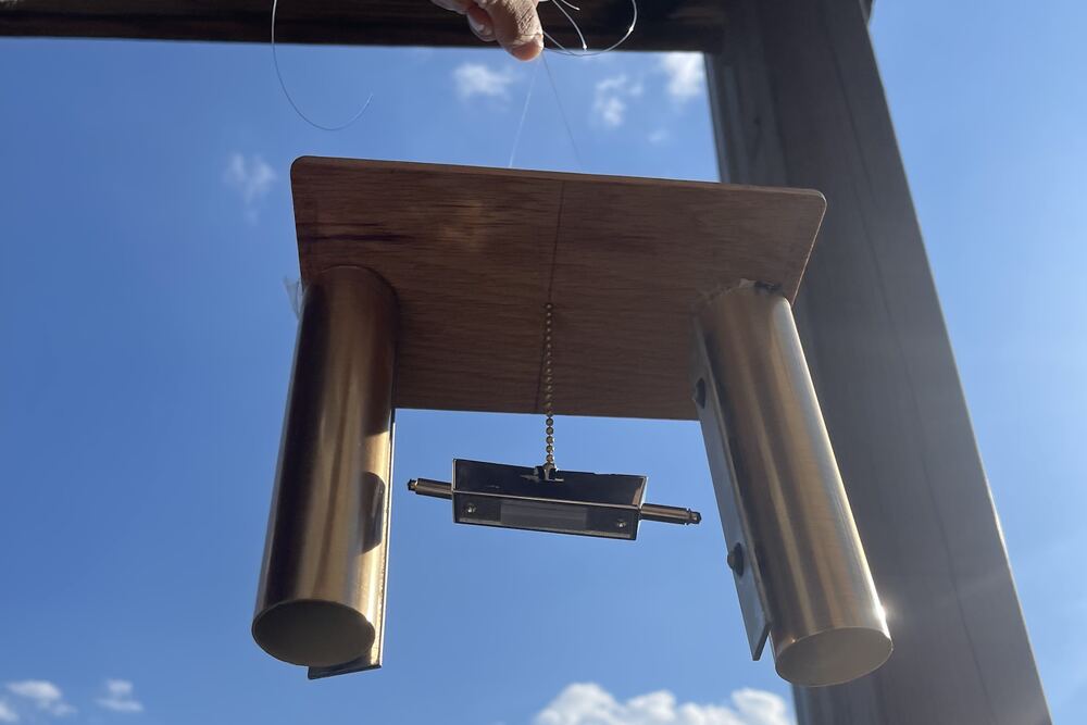 The chime held up by a thread against a blue sky, the striker hanging between the two tubes