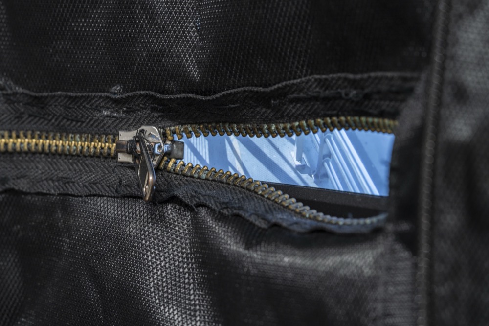 A screen glowing through the open zipper of a black backpack