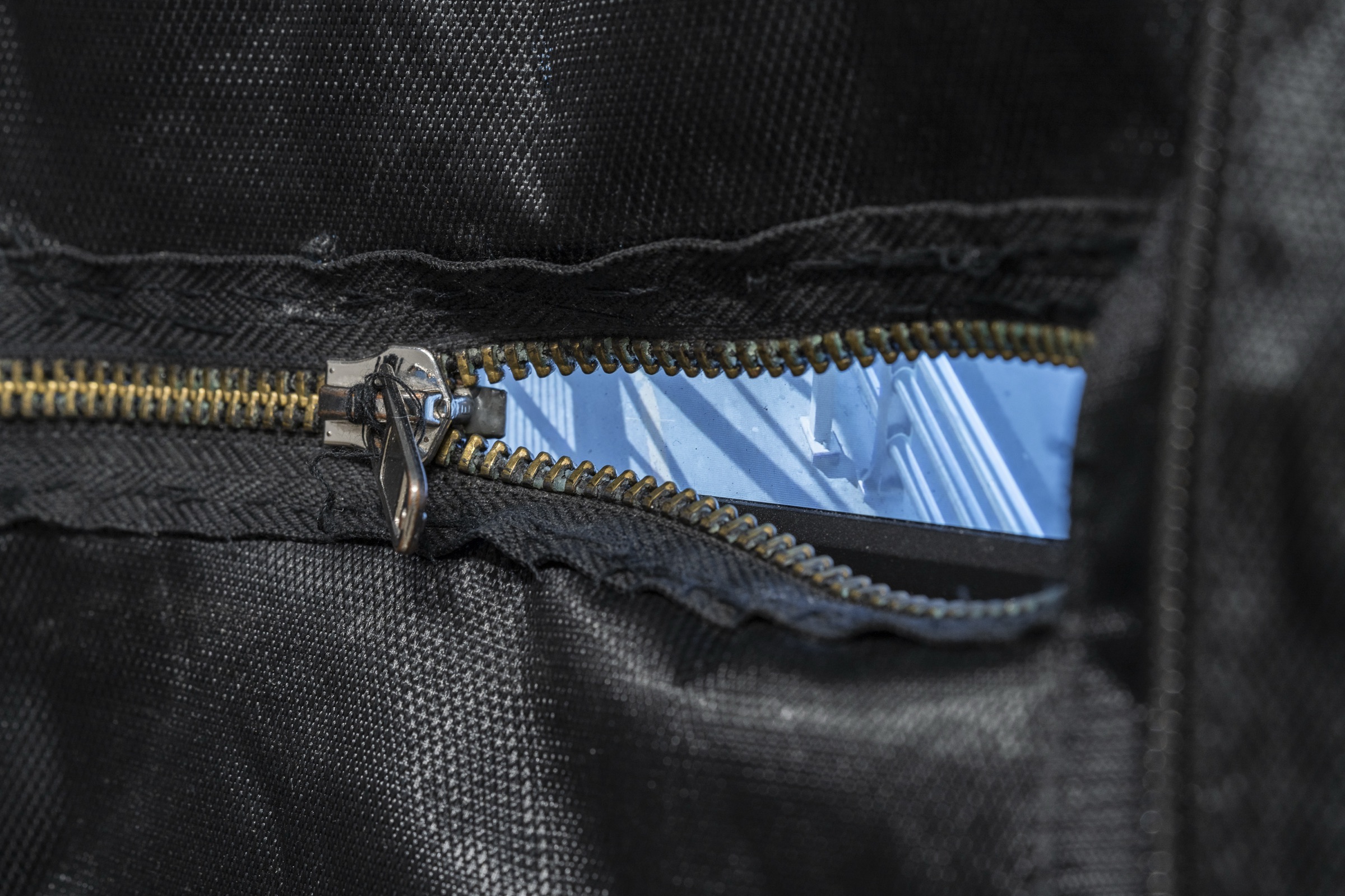 A screen glowing through the open zipper of a black backpack