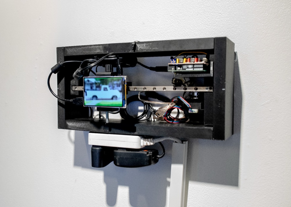 The frame on a white wall: the screen on a metal rail beside a circuit board and wiring