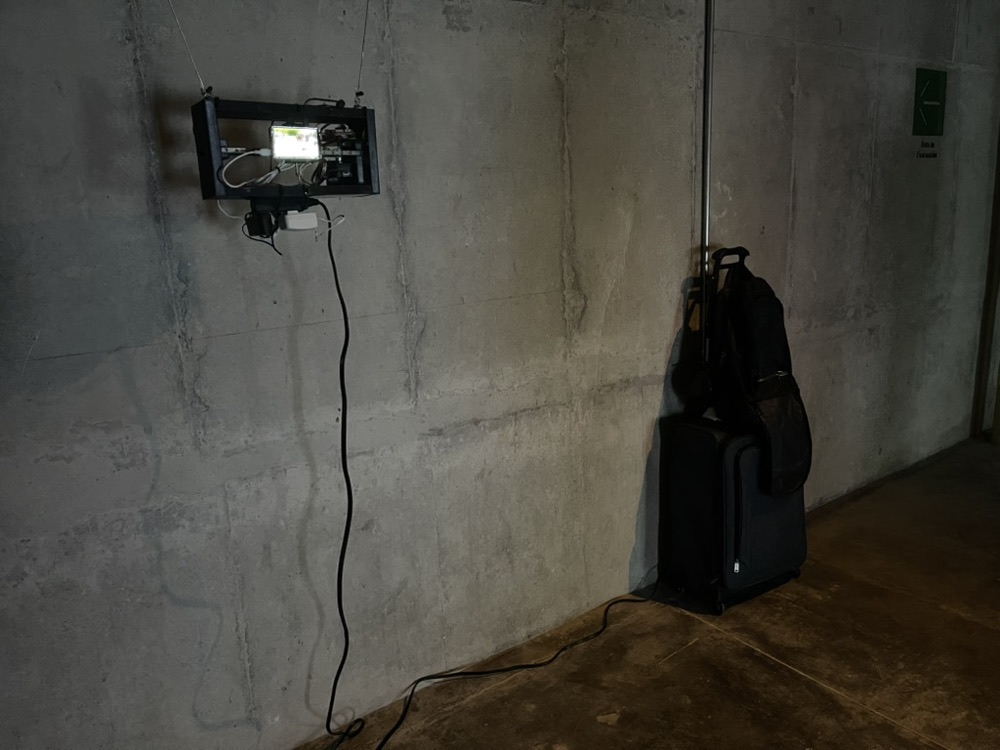 The piece on a long concrete wall, its cable running down to the floor